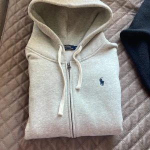 Grå hoodie från Polo Ralph Lauren - Säljer en klassisk grå hoodie från Polo Ralph Lauren i storlek L men passar m snvlnd 2 gånger, hoodein är i nytt skick har inga defekter eller något. På bilderna är jag 180 och väger cirka 75 kg