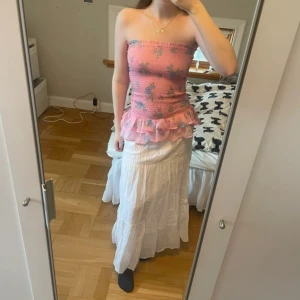 Rosa blommig bandeau tubtopp/kjol med volang - Supersöt rosa bandeau tubtopp/kjol med blommigt mönster i lila och grönt. Toppen är smockad och har en volangkant nertill i transparent tyg. Perfekt för sommarens alla tillfällen och ger en romantisk vibe. Går att använda som både topp och kjol😍💞