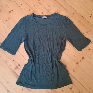 Mörkgrön topp från Filippa K - En stilren mörkgrön topp från Filippa K i mjuk bomull. Modellen har rund halsringning och halvlånga ärmar som ger en clean och enkel look. Perfekt för dig som gillar minimalistisk stil och vill ha något som funkar till många outfits.