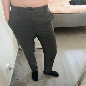 Grå kostymbyxor från Boomerang - Snygga grå kostymbyxor från Boomerang i klassisk modell med normal passform. Byxorna har hög midja, bälteshällor och knäppning fram. Materialet känns mjukt och är troligtvis ullblandning, perfekt för en clean och stilren look.