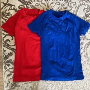 Röd och blå t-shirt i stretch, Shein - Två t-shirts i storlek S, en röd och en blå. Båda är kortärmade och har en enkel, tight passform med ribbade muddar nedtill. Materialet är stretchigt och består av 92% polyamid och 8% elastan, vilket gör dem mjuka och följsamma. Perfekta för en sportig och clean look. Från Shein 