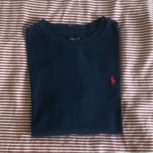 Mörkblå t-shirt från Polo Ralph Lauren - Snygg mörkblå t-shirt från Polo Ralph Lauren med klassisk röd broderad logga på bröstet. T-shirten är i mjuk bomull och har en normal passform med korta ärmar och rund halsring.