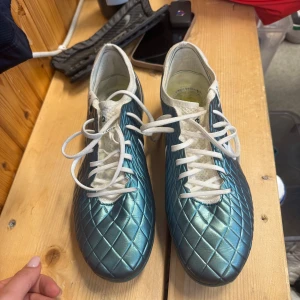 Nike Tiempo Metalic  - Snygga Nike fotbollsskor i metallicblått med rutmönstrad ovandel och vita detaljer. Skorna har vita snören, vit sula och inslag av mesh vid öppningen för extra komfort. Perfekta för dig som vill sticka ut på planen. Använda 2 gånger! Nypris 3100kr,2024 årsmodell .