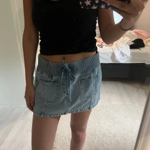 Blå jeanskjol med snörning - Blå kort jeanskjol med brett ribbad band i midjan midja och snörning framtill