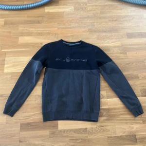 Svart Sail Racing sweatshirt - Snygg svart sweatshirt från Sail Racing med diskret logga framtill. Tröjan har rund halsringning och långa ärmar. Den är tillverkad i mjukt material och har en stilren tvådelad design med mörkare och ljusare svarta partier. Perfekt för en clean och sportig look. Pris kan diskuteras.