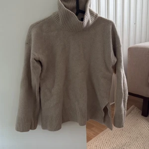 Beige polotröja från GANT i ull - Säljer en beige polotröja från GANT i storlek L, men är i storlek som en xs. Tröjan är stickad i mjuk ull och har en hög, ribbad polokrage samt ribbade muddar vid ärmslut och nederkant. Perfekt för lager-på-lager under kyliga dagar.