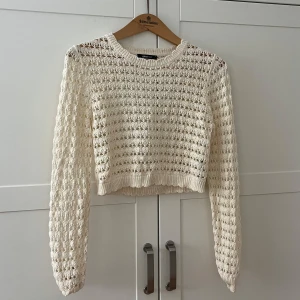 Vit stickad croppad tröja med öppen rygg - Superfin vit stickad tröja från Gina Tricot med croppad passform och lång ärm. Tröjan har ett snyggt hålmönster och en stor öppen rygg som ger en unik look. Perfekt att styla med höga jeans eller kjol. Prislapp kvar