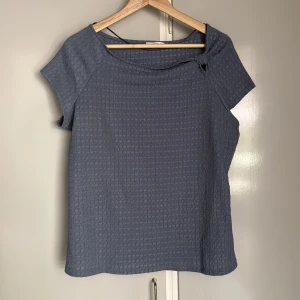 Blå topp med knut från Encuentro Large - Säljer en blå topp från Encuentro i storlek L. Toppen har korta ärmar, diskret rutstruktur i tyget och en snygg knutdetalj vid halsringningen. 