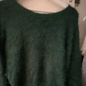 Mörkgrön fluffig stickad tröja - Mysig mörkgrön stickad tröja med fluffig yta och rund hals. Perfekt för dig som gillar oversized och sköna plagg med lite extra attityd. Passar till både jeans och kjol för en chill look.