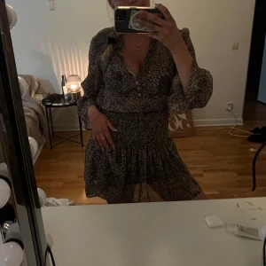 Leopardmönstrad kortklänning med volang - Säljer en kort, luftig klänning med leopardmönster och volangkant. Klänningen har v-ringning med knappar framtill och långa, transparenta ärmar. Perfekt för dig som gillar djurmönster och en avslappnad men trendig look.