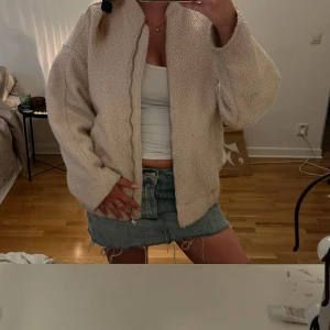 Beige teddyjacka med dragkedja - Supermysig beige teddyjacka med oversized passform och hög krage. Jackan har en hel dragkedja framtill och är gjord i fluffigt teddy-material som håller dig varm. Perfekt att slänga på sig när det är kyligt ute. Enkel och stilren design utan synliga loggor.