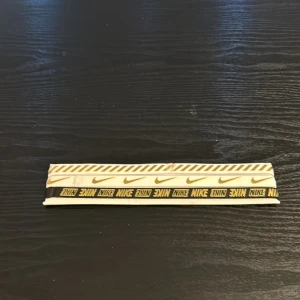 Nike vit och gul randigt hårband 3 pack - Snyggt bälte från Nike i beige med gula detaljer. Bältet har ett randigt mönster upptill, Nike-loggor i mitten och en svart remsa med gul Nike-text längst ner. Perfekt accessoar för att lyfta din outfit med sportig vibe.