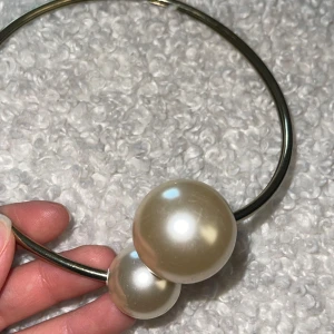 Halsband med stora pärlor - Snyggt stelt halsband i silverfärgad metall med två stora, glansiga pärlor i vitt. Halsbandet har en minimalistisk och modern design som sticker ut med sina överdimensionerade pärldetaljer. Perfekt för dig som gillar statement-smycken.