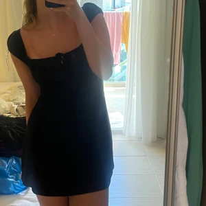 Svart kort klänning med snörning framtill - Snygg svart kort klänning med söt snörningsdetalj framtill och puffiga axelband. Klänningen har en enkel, figurnära passform och är perfekt för dig som gillar en stilren look. Passar lika bra till sneakers som till klackar.