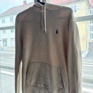 Stickad beige hoodie från Polo Ralph Lauren - Beige stickad hoodie från Polo Ralph Lauren med klassisk broderad logga på. Samma tröja som Marcus Rolf har på bilden