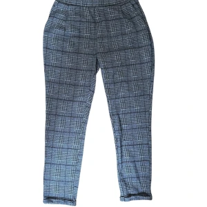 Grå rutiga kostymbyxor - Snygga grå kostymbyxor med svartvitt rutmönster. Byxorna har hög midja, smal passform och raka ben. Perfekta för en clean och stilren look. Tillverkade i ett mjukt material som känns bekvämt hela dagen.