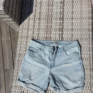 Ljusblå jeansshorts från Denim Co. - Snygga ljusblå jeansshorts från Denim Co. med slitna detaljer och upprullade benslut. Klassisk femficksmodell med dragkedja och knapp framtill. Perfekta för varma dagar och en avslappnad stil.