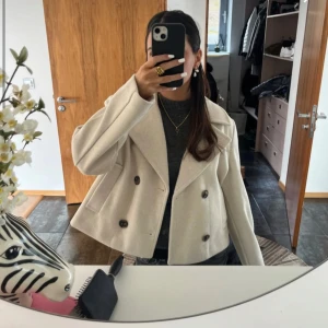 Beige croppad skepparkavaj - Snygg beige skepparkavaj med croppad passform och breda slag. Jackan har dubbelknäppning med stora mörka knappar och långa ärmar. Perfekt för dig som gillar stilrena och trendiga plagg med lite edge.