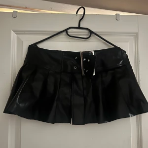 Svart minikjol i skinnimitation med bälte - Snygg svart kortkjol i skinnimitation med bredt bälte och silverspänne. Pris kan diskuteras 🥰