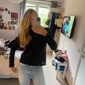 Svart paljettopp från Vero Moda - Säljer en svart långärmad topp från Vero Moda, täckt med glittriga paljetter. Toppen har en rak passform och dragkedja i ryggen för enkel på- och avtagning. Perfekt för dig som vill sticka ut med lite extra glitter.