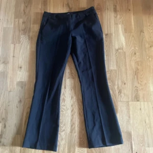 Svarta bootcut kostymbyxor BikBok 36 - Svarta kostymbyxor från BikBok i storlek 36. Byxorna har bootcut-ben, lågmidja och klassisk passform med hällor för bälte och diskreta bakfickor. Perfekta för en clean och stilren look. Materialet är mjukt och följsamt, vilket gör dem bekväma hela dagen. Dom är petite alltså kortare längden 