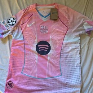 Barcelona Lamine Yamal 10 rosa Nike tröja - Snygg FC Barcelona fotbollströja från Nike i rosa och vita toner med Lamine Yamal och nummer 10 på ryggen. Tröjan har korta ärmar, coolt randigt mönster och detaljer som Spotify-logga och Champions League-patch. Tillverkad i lätt, ventilerande Dri-FIT-material. Köpt i Spanien på semester så antar att den inte är äkta! Den är helt oanvänd 