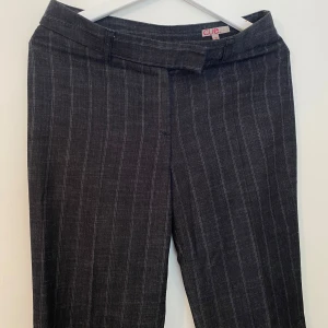 Randiga kostymbyxor från Cue - Snygga mörkgrå kostymbyxor från Cue med tunna vita ränder. Byxorna har en trendig och smickrande passform. 
