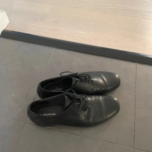 Loafers från Vagabond som NY - Snygga svarta loafers från Vagabond i äkta skinn med klassisk rund tå och platt sula. Skorna har stilren design med snörning och passar perfekt till dig som gillar en clean och tidlös look. Perfekta att matcha med både jeans och kostym.