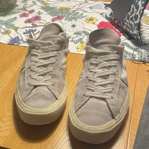Gråa sneakers från Tom Ford i mocka - Snygga beige sneakers från Tom Ford med ovandel i mocka och vita detaljer på sidorna. Klassisk låg modell med snörning och rund tå. Sulan är i gummi och har Tom Ford-logga baktill och undertill. Perfekta för dig som gillar stilrena och exklusiva sneakers. Ej fast pris