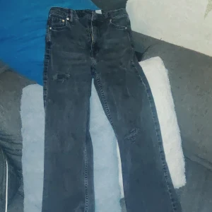 Bootcut high waist jeans från &Denim - Snygga svarta bootcut jeans från &Denim med hög midja. Jeansen har slitna detaljer på benen och klassisk femficksdesign. Perfekta för dig som gillar en lite retro vibe och vill ha ett par jeans som sticker ut.