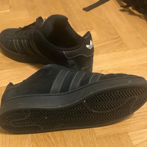 Svarta Adidas Campus sneakers mocka - Säljer min sons svarta Adidas Campus sneakers i mocka med klassiska tre ränder på sidan och vit Adidas-logga på hälen. Skorna har rund tå, platt sula och snörning. Sparsam använda. Köpta förra året på JD i Mall of Scandinavia. Mycket bra skick nästan som nya. Storlek 44 2/3