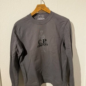C.P. Company tröja - Snygg grå sweatshirt från C.P. Company med tryckt motiv av en person och tydlig logga på bröstet. Storlek S