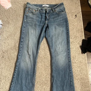 Blå bootcut jeans från junkyard - Snygga blå jeans från Junkyard med klassisk femficksdesign och bootcut-ben. Jeansen har ljus tvätt med slitningar och kontrastsömmar på bakfickorna. Tillverkade i jeansmaterial med dragkedja och knapp framtill. Perfekt för dig som gillar retrovibe och avslappnad stil.