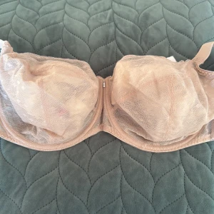 Beige bh från Freya - Säljer en beige bh från Freya med vacker spets och transparenta detaljer. Bh har justerbara axelband och hakknäppning bak. Perfekt för dig som gillar en feminin och stilren look. Materialet är mjukt och följsamt för extra komfort.