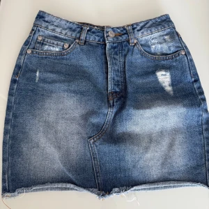 Blå jeanskjol med slitningar - Snygg blå jeanskjol med slitna detaljer och rå kant nertill. Använt några enstaka gånger 