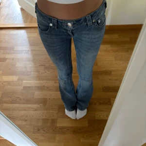 True Religion bootcut jeans blå - Säljer ett par snygga blå jeans från True Religion med bootcut passform och låg midja. Jeansen är lågmidjade men lite långa i benen så dem är lite slitna. 