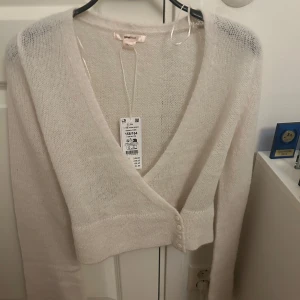 Ljusbeige kofta från Gina Tricot - Supermjuk och fluffig ljusbeige kofta från Gina Tricot. djup v-ringning och fina knappar framtill. Långärmad och stickad i ett lätt material som känns lyxigt och passar perfekt till lager-på-lager.