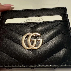 Svart GG kortfodral i skinn - Snygg svart plånbok/korthållare med GG-logga i guld på framsidan. Plånboken är tillverkad i falsk skinn och har quiltad design med flera fack för kort. Helt ny, den är INTE rostig det är bara ljuset!🩷