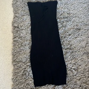 Svart ribbad långkjol från Primark - Svart ribbad långkjol från Primark med snörning i midjan och en snygg slits bak. Kjolen är stickad och har en tight passform som framhäver siluetten. Perfekt för dig som gillar en stilren och enkel look.