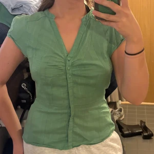 Tajt blus  - Snygg grön blus med korta ärmar och dekorativa knappar framtill. Figurnära passform.
