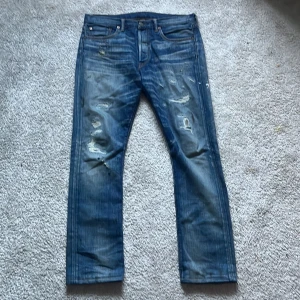 Blå RRL jeans med slitningar, stl 30 - Säljer ett par blå jeans från RRL med snygga slitningar och distressed detaljer framtill. Klassisk femficksmodell med läderpatch bak i midjan. Jeansen är raka i modellen och tillverkade i 100% bomull. Perfekta för dig som gillar en rå och avslappnad look. Priset kan diskuteras vid snabbt köp och fråga gärna frågor🙂