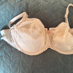 Begie bh från Chantelle - Supersöt beige  bh från Chantelle med tunna vertikala ränder och spetsdetaljer upptill. Dekorerad med en liten rosett i mitten och fina broderade kanter. Perfekt för dig som gillar romantiska och feminina detaljer.