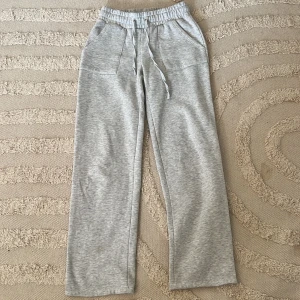 Grå mjukisbyxor från Lager 157 - Grå mjukisbyxor från Lager 157, modell Stella. Byxorna har resår och snörning i midjan, raka ben och stora fickor både fram och bak. 