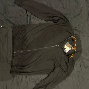 Svart zip tröja från HUGO BOSS  - Svart kofta från BOSS med ribbad krage och muddar, hel dragkedja framtill och diskret BOSS-logga på bröstet. Helt ny med lappen kvar. Storlek L
