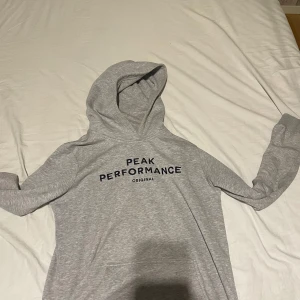 Grå hoodie Peak Performance 170 - Säljer en grå hoodie från Peak Performance i storlek 170. Tröjan har svart text på bröstet, huva och en klassisk känguruficka framtill. Mjuk insida och långa ärmar gör den perfekt för chill dagar. Passar dig som gillar enkel och stilren design. Nypris ca 700