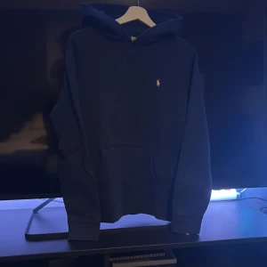 Mörkblå hoodie från Polo Ralph Lauren - Snygg mörkblå hoodie från Polo Ralph Lauren med klassisk broderad logga på bröstet. Tröjan har huva,  och långa ärmar. Perfekt för en chill och stilren look. Tillverkad i mjuk bomull för extra komfort. mycket bra skick, hör av dig! 