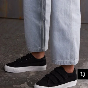 Svarta sneakers med kardborreband - Stilrena svarta sneakers med bred vit sula och tre kardborreband. Skorna har en rund tå och är tillverkade i manchestertyg som ger en cool textur. Perfekta för en avslappnad streetstyle-look, använd ett par gånger och är lite smutsiga