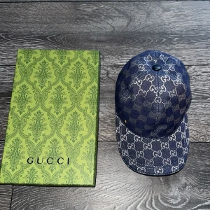 Gucci blå keps med GG-mönster - Snygg blå keps från Gucci med klassiskt GG-mönster över hela kepsen. Kepsen har böjd skärm och kommer med originalförpackning och dustbag. Den är även helt ny