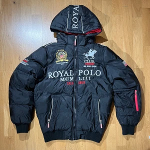 pufferjacka Geographical Norway - Svart pufferjacka från Geographical Norway med broderade detaljer och tryck på bröstet och ärmarna. Jackan har huva, röda dragkedjor och fodrad insida i rött. Perfekt för kalla dagar med sin sportiga och streetiga vibe. Såg att nya kostar runt 6000kr. Royal polo. Äkta. Mer information, bilder och prisdiskutering i dm. Passar M
