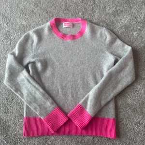 Grå stickad tröja  med rosa detaljer - Supermjuk grå stickad tröja från From Future med ribbade detaljer i knallrosa vid hals, ärmslut och nederkant. Klassisk rund halsringning och långärmad modell som är både snygg och bekväm. Säljer för den inte passar så bra💕